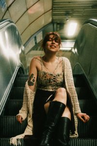 young-woman-with-tattoos-sitting-on-an-escalator-looking-at-the-camera-F100038756